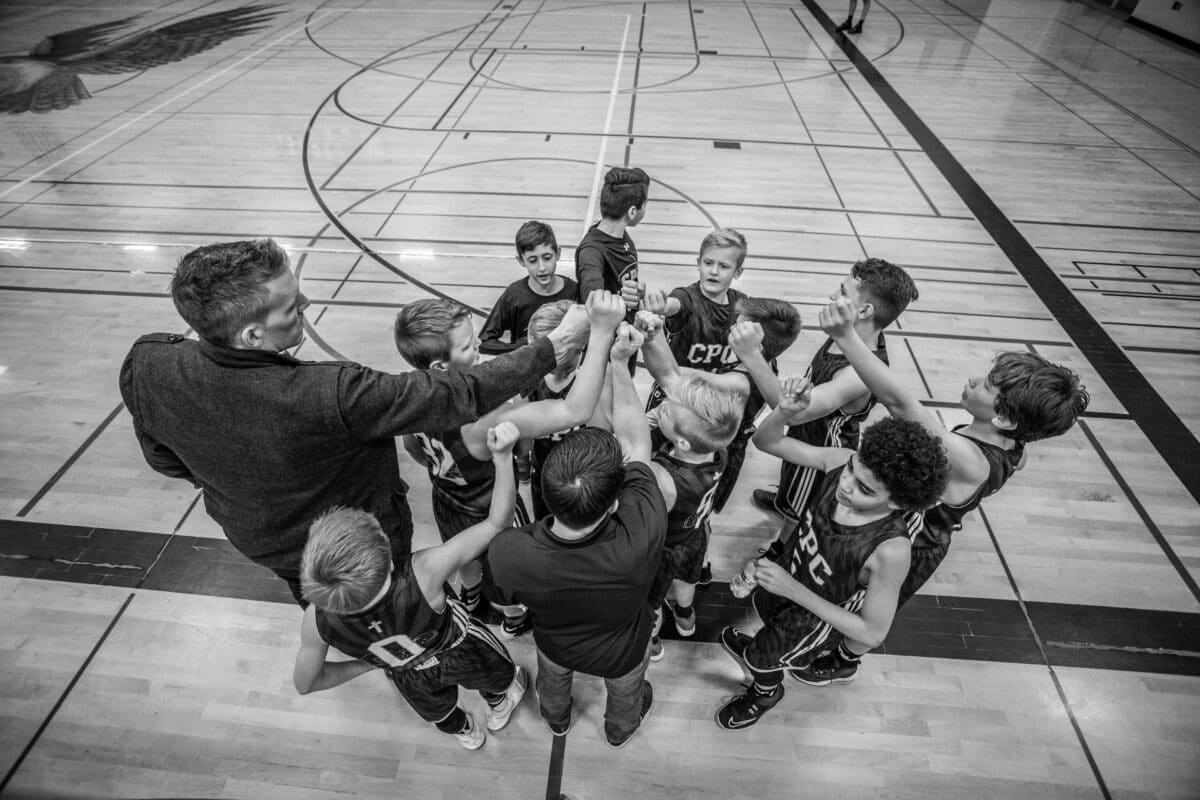 black and white aerial image of a coach leading a huddle of a kid's basketball team.