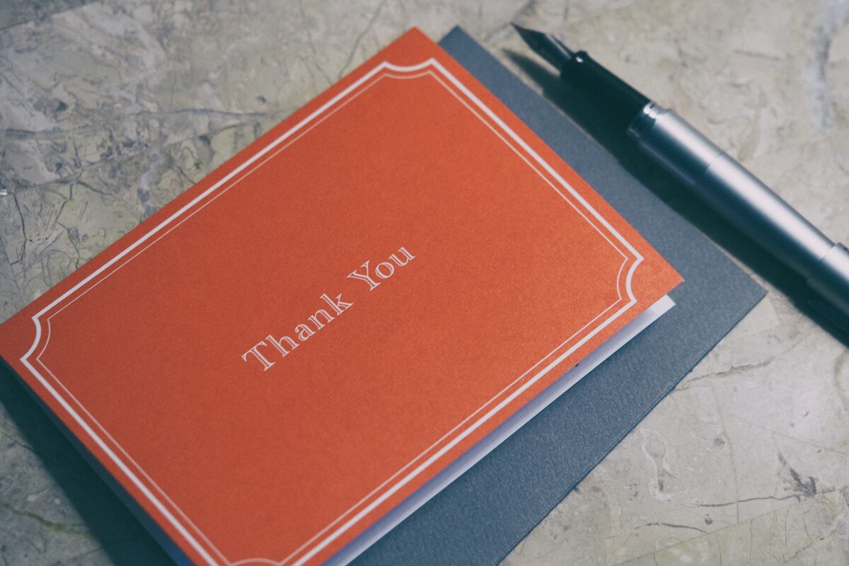 Red thank you card and gray envelope on a flat surface next to a fancy pen